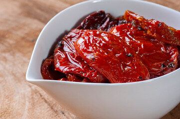 .Sun-dried tomatoes in a white bowl on a woody background.