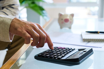 Selective focus of Asian men hand while calculate for personal saving with document and piggy bank...