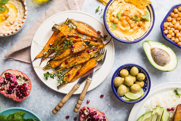 Variety of healthy vegan snacks, gourmet dips. Hummus,  roasted carrots, rice with tempeh in ceramic bowls viewed from above, plant based food