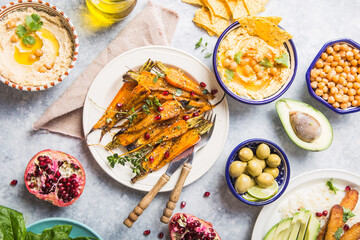 Fototapeta na wymiar Variety of healthy vegan snacks, gourmet dips. Hummus, roasted carrots, rice with tempeh in ceramic bowls viewed from above, plant based food