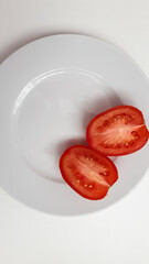 Two halves of red tomato on a white plate without patterns. Top view. Ripe, healthy, tasty lunch or main meal. Minimalism. White background for text. White porcelain round plate.