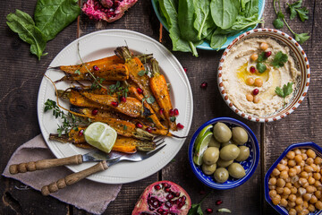 Variety of healthy vegan snacks, gourmet dips. Hummus,  roasted carrots, rice with tempeh in ceramic bowls viewed from above, plant based food
