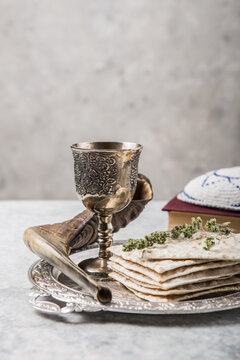 Metal plate with matzah or matza, Kiddush Cup, Shofar horn on a light  background presented as a Passover seder feast or meal with copy space. Jewish traditional objects, yarmulke, Tallit, Prayer book