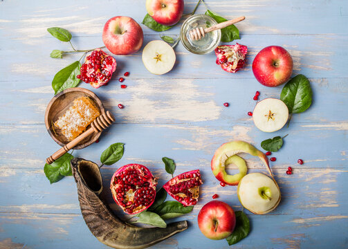 Rosh hashanah  (Hashana) - jewish New Year holiday concept. Traditional symbols: Honey jar and fresh apples with pomegranate and shofar - horn on a blue background.  View from above