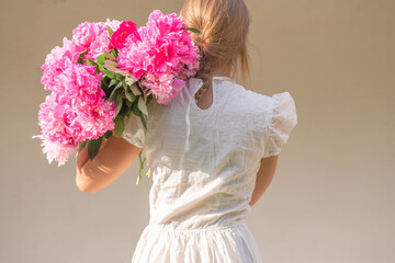 Boho girl holding pink peonies in straw basket. Stylish hipster woman in bohemian floral dress gathering peony flowers on white backgrounds. International Womens Day. Wedding decor and arrangement