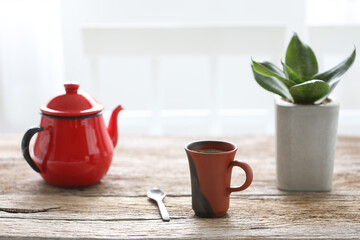 Red coffee cup and teapot with snake plant on brown rustic wooden table 
