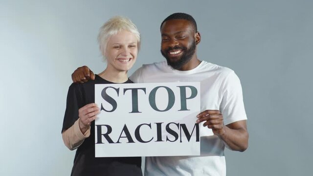 Close up happy white woman and African american man hold poster Stop Racism look at camera smiling racial morality society peace matter human text words can kill torture slow motion