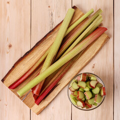 Pile of freshly cut pieces of sour rhubarb in glass bowl on a wooden table. Cultivated plant, which eaten as a fruit after cooking.