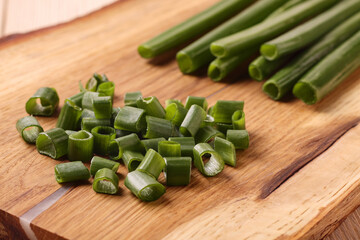 Chopped green onion and onion stalks on wooden board on table.