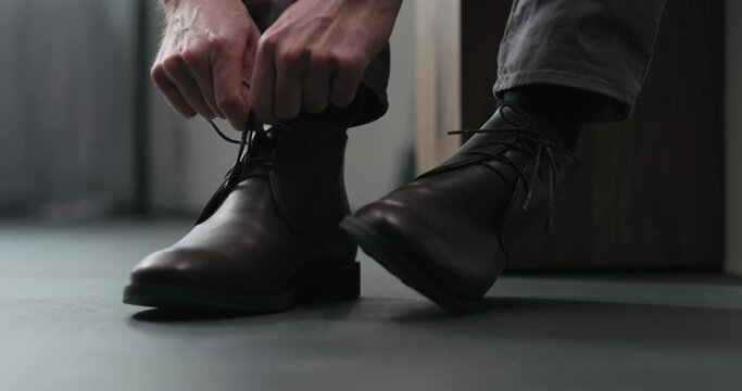 Slow motion man lace up his brown leather chukka boots indoor
