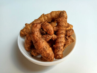 Turmeric or Curcuma longa rhizomes in a bowl, isolated in white background