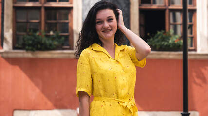 Portait of Beautiful Young Lady Wearing Yellow Dress Curly Hair Looking Happy. Young Attractive  woman smiling happy and confident. Standing at town street.