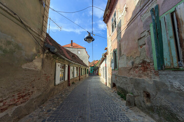 SIBIU, ROMANIA - Circa 2020: Old medieval town brick wall with cloudy blue sky. Beautiful tourist spot in eastern central Europe. Narrow old street with damaged houses. Damaged house concept.
