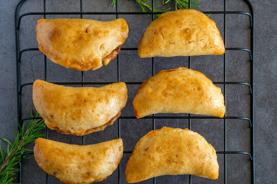 Top view on homemade freshly baked empanadas pastry with meat filling a gluten-free version of an authentic traditional Spanish Latin America cuisine food on a black cooling rack