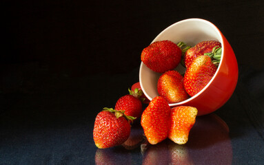 Strawberries in cup on black background and table with reflection