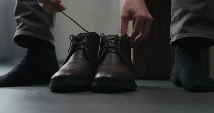 Slow motion young man put on his brown leather chukka boots indoor