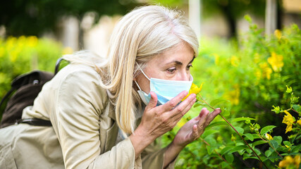 Woman trying to smell flower while wearing a mask, coronavirus pandemic concept