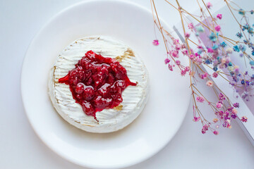Camembert cheese baked with berry sauce on the background of a magazine, decorated with a flower branch. Bright fluorescent light. The view from the top