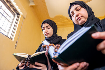 Muslim mother and her daughtersitting togther reading holy book