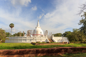Panoramic view of restored Thuparamaya Dagoba with white bell shaped Stupa, altars, tilted vatadage pillars and Buddhist flags, Anuradhapura, Sri Lanka. Beautiful cloudy sky landscape.