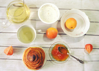 Healthy breakfast on the table with green tea cup, glass teapot, fresh apricots, apricot jam,  twist of bread, skyr. Healthy life style. Food still life. Top view