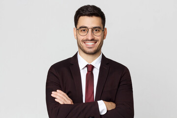 Smiling businessman wearing round glasses, dressed in burgundy suit, white shirt and red tie, looking at camera, isolated on gray background