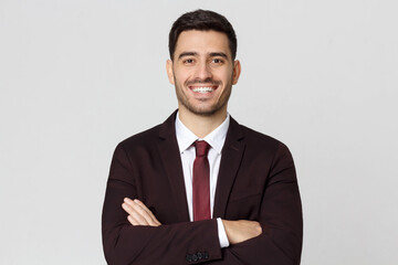 Smiling young manager wearing dressed in burgundy suit, white shirt and red tie looking at camera, isolated on gray background