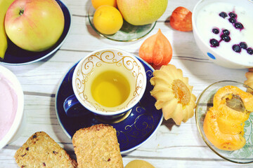 Healthy protein- and vitamin-rich breakfast on the table with green tea cup,  vanilla chia pudding made of skim milk, apple, apricots, banana, pear, skyr with blueberries, cereal cookies. 