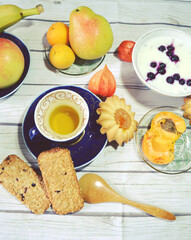 Healthy protein- and vitamin-rich breakfast on the table with green tea cup,  vanilla chia pudding made of skim milk, apple, apricots, banana, pear, skyr with blueberries, cereal cookies. 