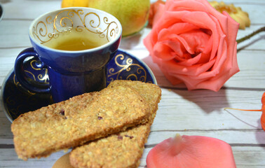 Green tea cup with a beautiful rose and cereal cookies on the table for healthy and romantic breakfast or lunch. Closeup. 