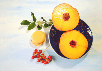 Rich fresh peach in slices on indigo blue plate and peach macaron against light-blue wooden table....