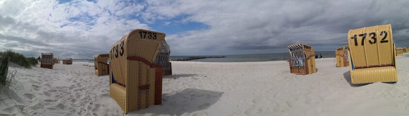 Sandy beach panoramic view with hooded beach chairs under overcast sky