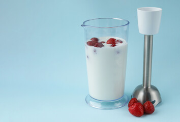 Natural yogurt and fresh strawberries in a tall glass and a blender on a blue background. Healthy and delicious food. Diet. Selective focus. Summer treat. Copy space