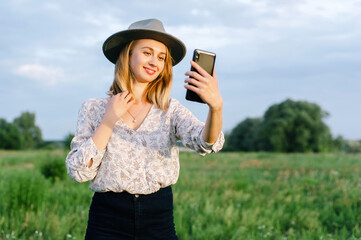 Young woman on nature using smartphone for selfie or speaking with her friends or relatives. Image for business, people, portrait, mobile and expression concept