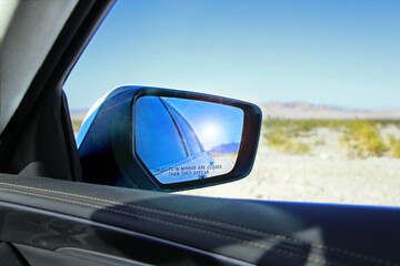 Car rear-view mirror with sun reflection with warning "Objects in mirror are closer than they appear" - view on the landscape in Death valley National Park from car window