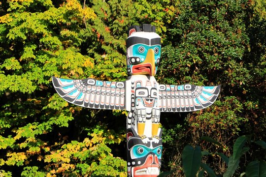 Beautiful painted colorful totem pole top detail - eagle's head with spread wings and the monkey, made by indigenous / native people of Canada, in Stanley park, Vancouver BC.