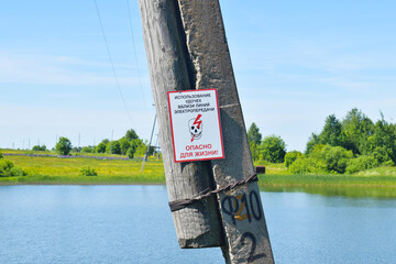 Russian sign on a pole for fishermen with a warning about the danger. Wooden post near the lake