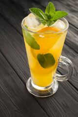 Orange drink or lemonade with mint and ice  in the glass  on the black wooden background. Closeup. Location vertical.