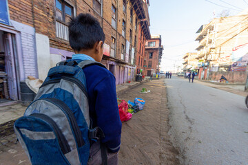 Kathmandu, Nepal - CIRCA 2020: Nepal, Kathmandu kid walking on an unpaved street to school with his back pack in the back. Concept of poverty schooling.