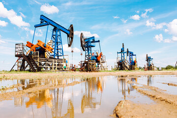 Fototapeta na wymiar Oil and gas industry. Working oil pump jack on a oil field with reflection on a puddle. White clouds and blue sky. Oil production