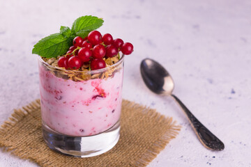 
A glass of yogurt with granola and red currant berries on a white background.