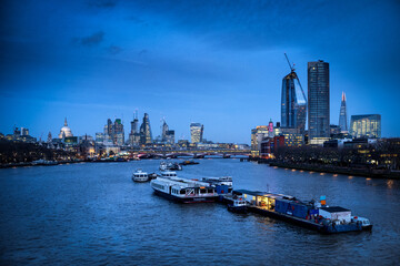 Fototapeta na wymiar The view of the City of London and The South Bank with the river Thames and the boats during the evening blue hour.