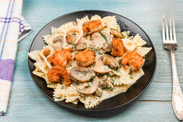 Farfalle with cream sauce with calamari and mushrooms and fried shrimps in a black plate - traditional Italian pasta with seafood and mushrooms, close-up