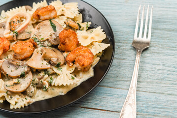 Farfalle with cream sauce with calamari and mushrooms and fried shrimps in a black plate - traditional Italian pasta with seafood and mushrooms, close-up
