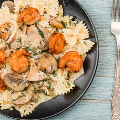 Farfalle with cream sauce with calamari and mushrooms and fried shrimps in a black plate - traditional Italian pasta with seafood and mushrooms, close-up