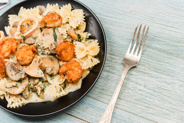 Farfalle with cream sauce with calamari and mushrooms and fried shrimps in a black plate - traditional Italian pasta with seafood and mushrooms, close-up