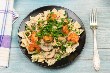 Farfalle with cream sauce with calamari and mushrooms and fried shrimps in a black plate - traditional Italian pasta with seafood and mushrooms, sprinkled with parsley, close-up