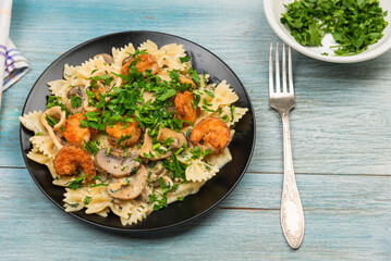 Farfalle with cream sauce with calamari and mushrooms and fried shrimps in a black plate - traditional Italian pasta with seafood and mushrooms, sprinkled with parsley, close-up