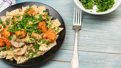 Farfalle with cream sauce with calamari and mushrooms and fried shrimps in a black plate - traditional Italian pasta with seafood and mushrooms, sprinkled with parsley, close-up