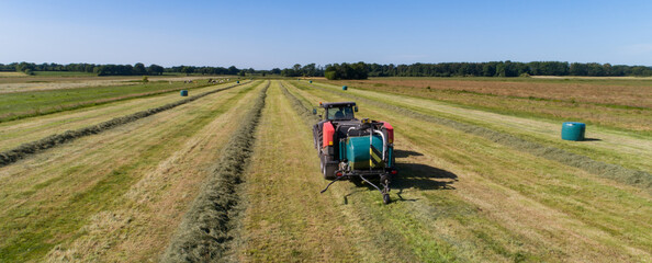 Schwarzer Treker mit einer roten Stroh Festkammerpresse bei der Strohernte auf einem gemähten Feld